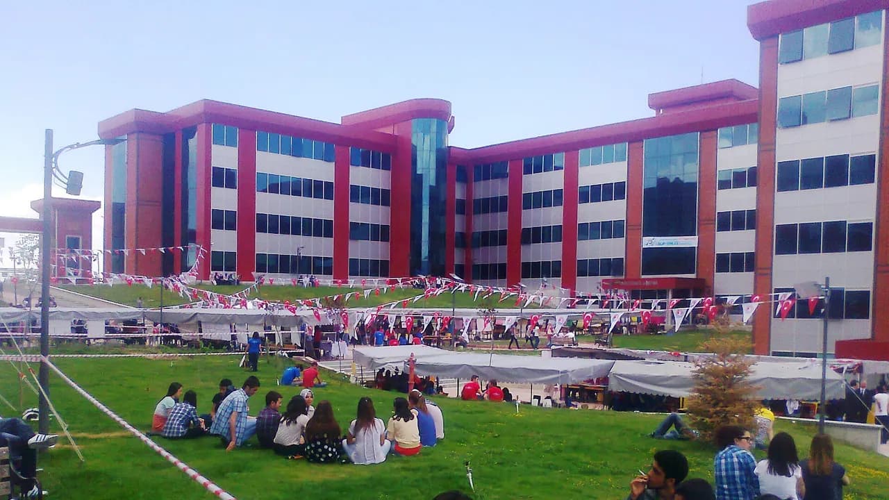 Burdur Mehmet Akif Ersoy Üniversitesi kampüsünde, bayraklarla süslenmiş çimenlikte oturup sohbet eden öğrenciler